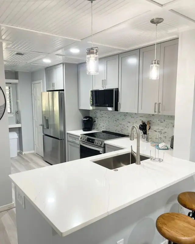 Remodeled kitchen with light gray shaker cabinets, white veined countertop, mosaic tile backsplash and glass pendant lights