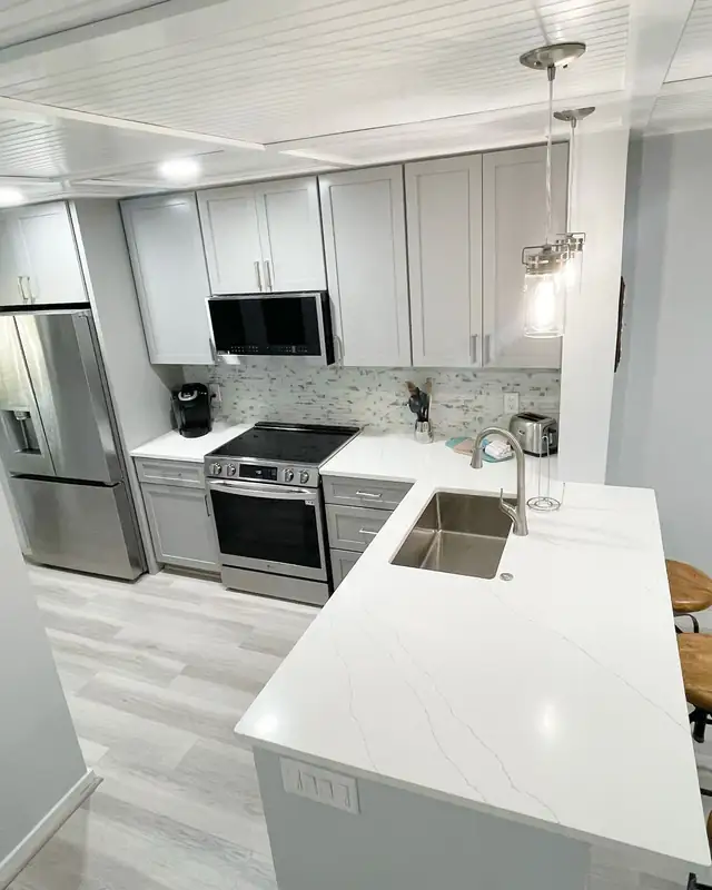 Kitchen peninsula with an undermount stainless sink, white veined countertop and light gray cabinets